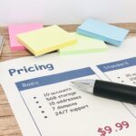 電卓と付箋の横に置かれた料金表にボールペンが添えられています。