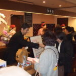 ガラポン抽選会が行われている賑わう温浴施設のフロントで接客するスタッフと客