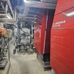 温浴施設のバックヤードに設置された赤い大型の潜熱回収温水器と配管設備