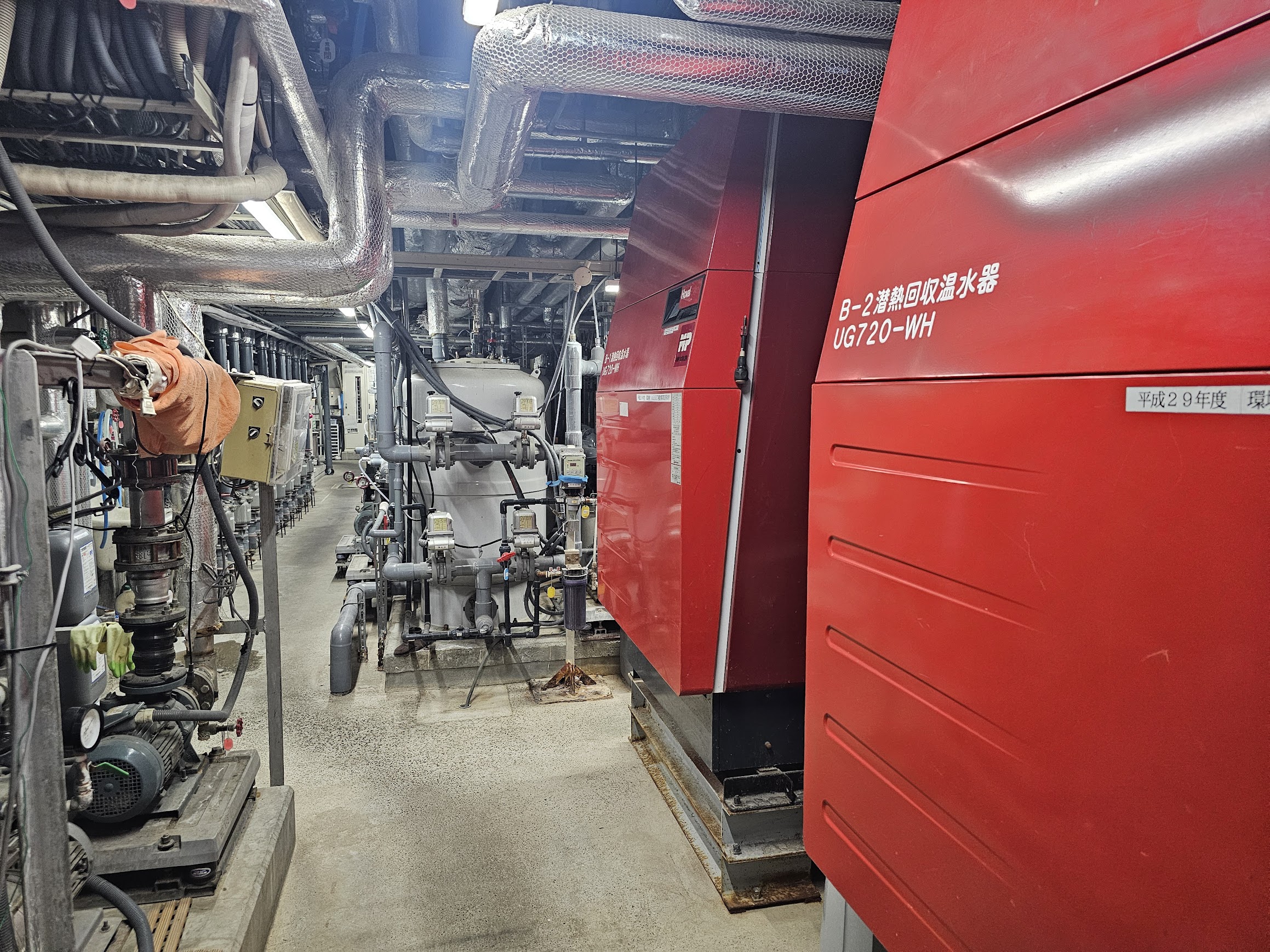 温浴施設のバックヤードに設置された赤い大型の潜熱回収温水器と配管設備