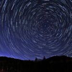 森林のシルエットの上で星の軌跡が円を描く夜空の風景