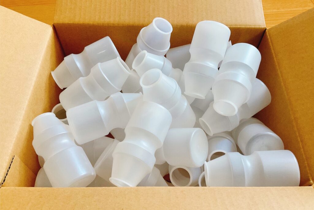 段ボール箱の中に温浴施設の集客事例に関わる大量の半透明の飲料向け空き容器が収められています。