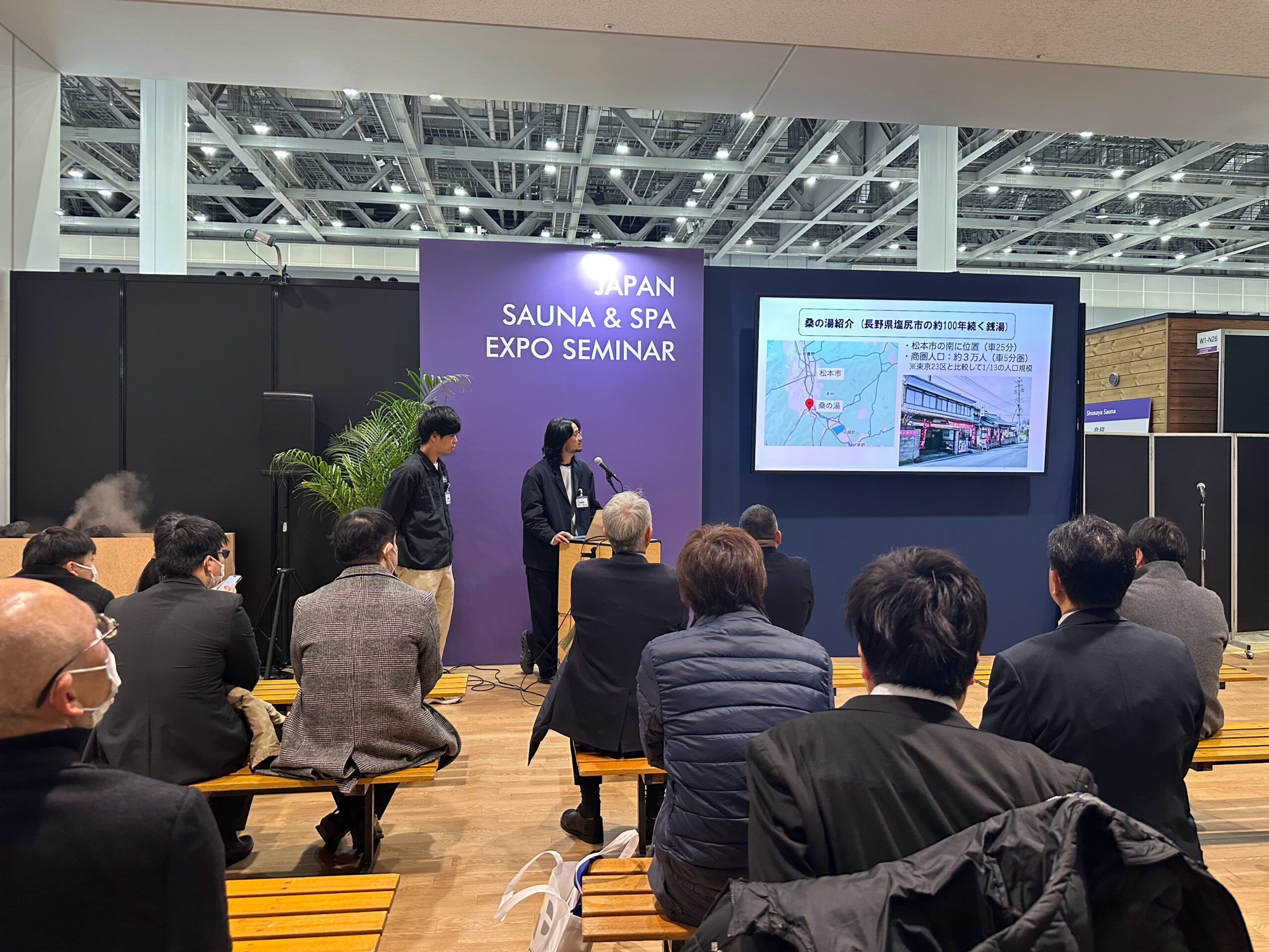 JAPAN SAUNA & SPA EXPOのセミナー会場で、スクリーンを使いながら講演を行う二人の登壇者とそれを見守る聴衆