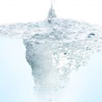 白い背景のなかで、上部から注がれた水が水面に激しい気泡を伴う渦を作り出している様子。