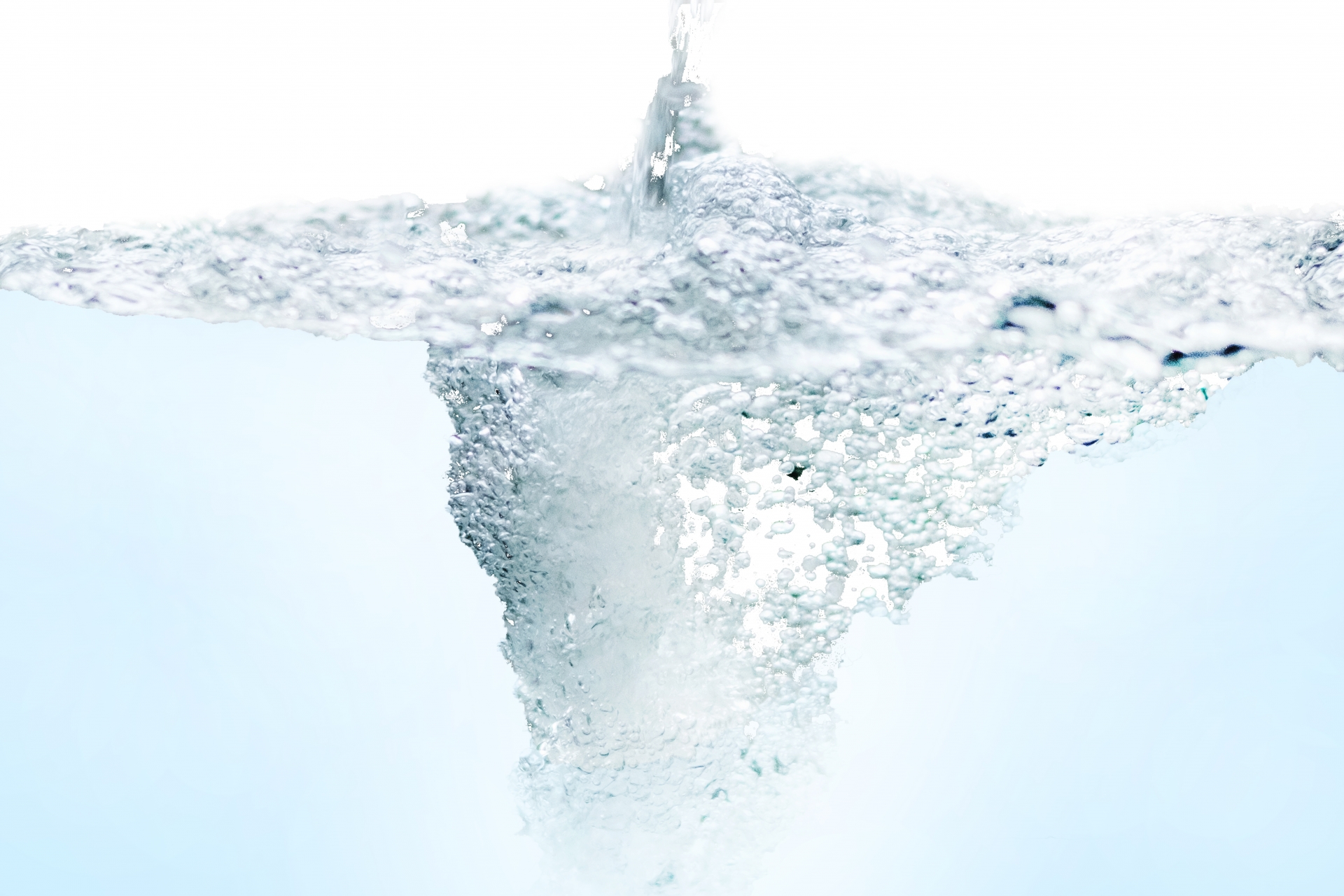 白い背景のなかで、上部から注がれた水が水面に激しい気泡を伴う渦を作り出している様子。