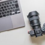 白いデスクの上に並べられたノートパソコンと黒いミラーレス一眼カメラの俯瞰写真です。