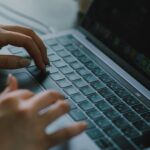 人物がノートパソコンのキーボードでタイピングをしています。