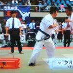 空手の試合で白の道着を着た二人の選手が間合いを取り合い、主審が見守る中で攻防を行う様子