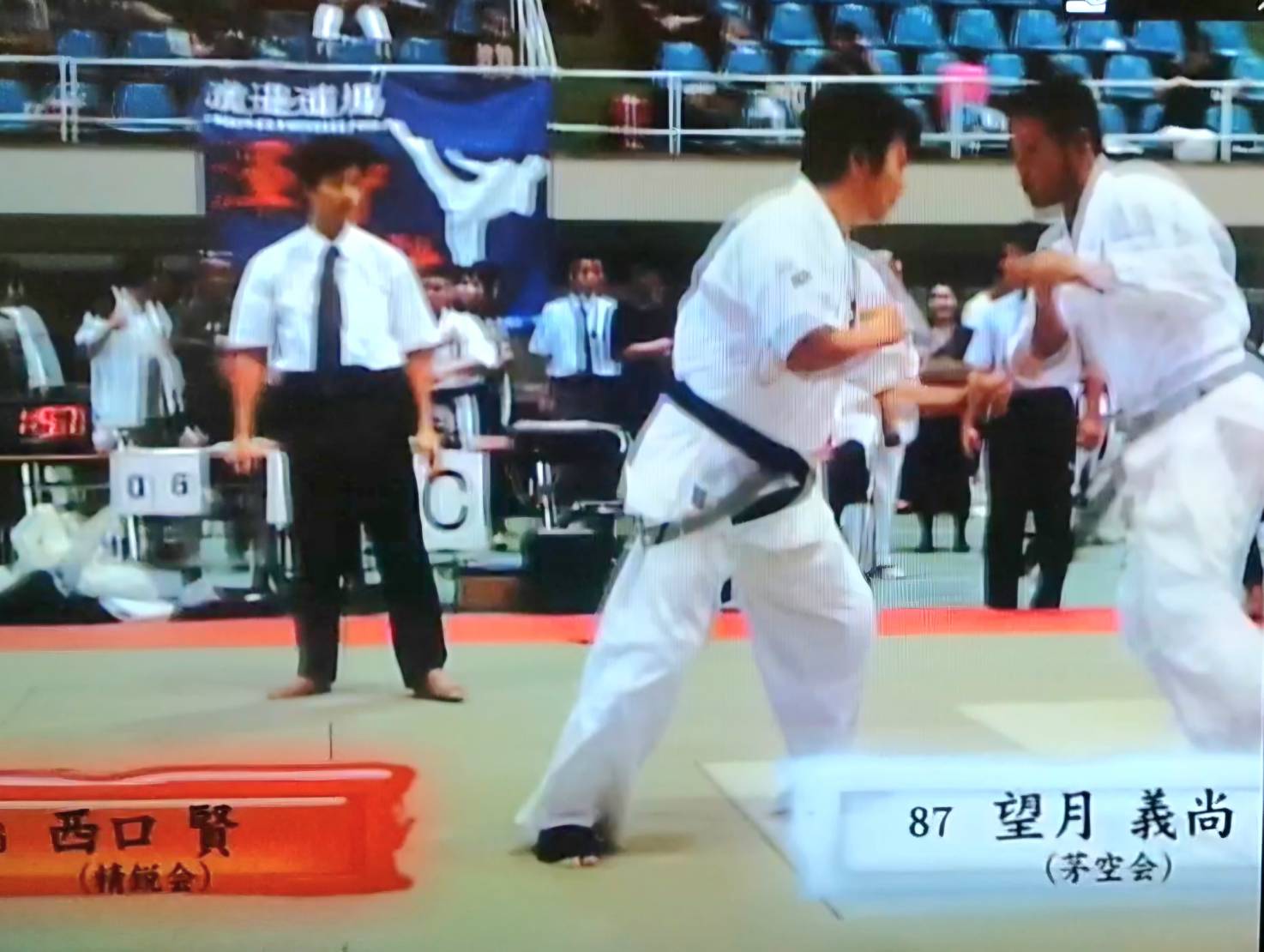 空手の試合で白の道着を着た二人の選手が間合いを取り合い、主審が見守る中で攻防を行う様子