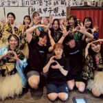 「熱波甲子園2026春」の看板を背景に、揃いの衣装を着たサウナ施設のスタッフたちが笑顔でポーズをとっています。