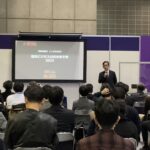 温浴ビジネスの近未来予測2023というスライドを背景にセミナーで講演する男性の様子。
