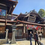 歴史ある木造建築の道後温泉本館の正面玄関前を歩く観光客の人々。