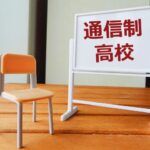 木目調のテーブルの上に置かれた小さな椅子と「通信制高校」と書かれたホワイトボードのミニチュア模型