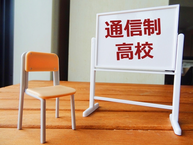 木目調のテーブルの上に置かれた小さな椅子と「通信制高校」と書かれたホワイトボードのミニチュア模型
