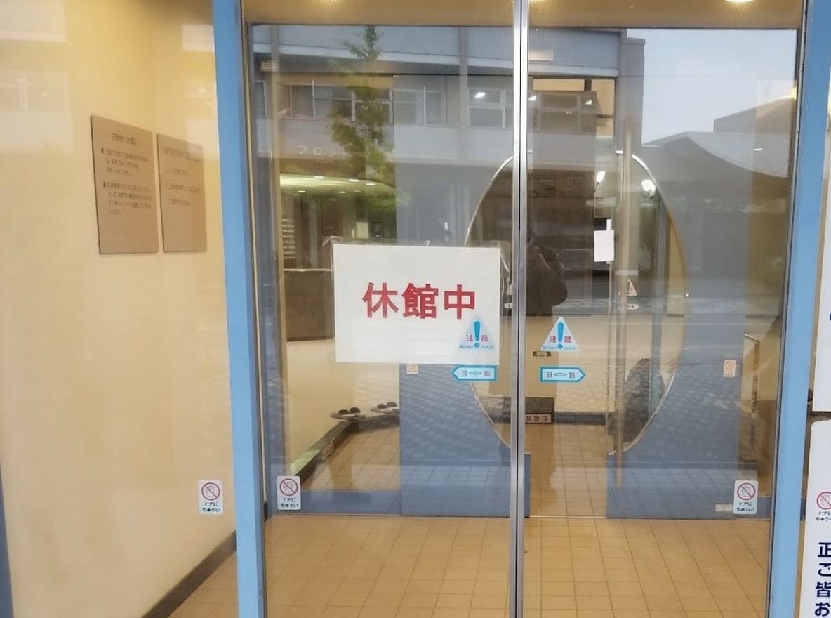 温浴施設のガラス張りの自動ドアに休館中と書かれた白い紙が貼り出されている様子