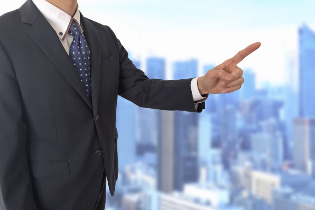 スーツを着たビジネスパーソンが右手で方向を指差し指示を出している様子