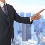 スーツを着たビジネスパーソンが右手で方向を指差し指示を出している様子