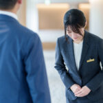 ホテルのロビーで男性客に向かってお辞儀をして謝罪するスーツ姿の女性スタッフ