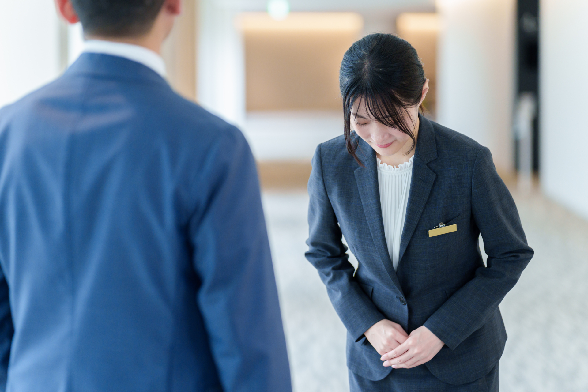 ホテルのロビーで男性客に向かってお辞儀をして謝罪するスーツ姿の女性スタッフ