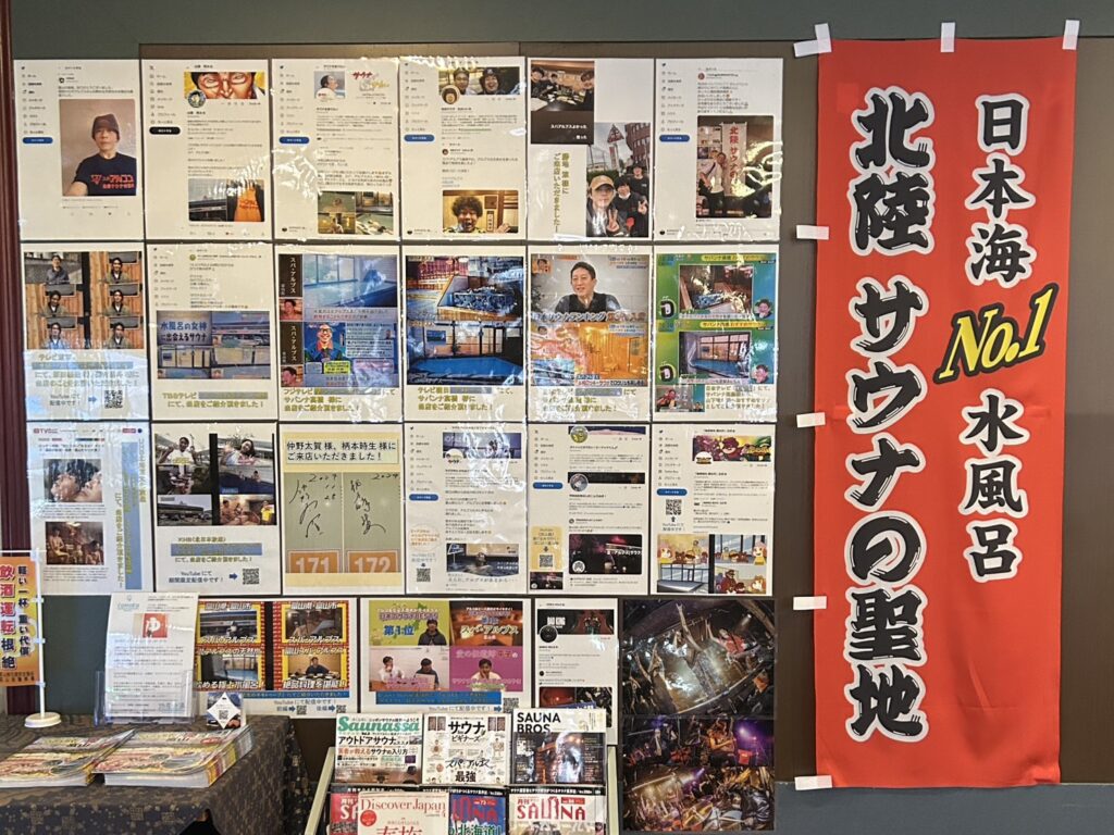 温浴施設の壁面にサウナや水風呂に関する多数の掲示物と赤い垂れ幕が飾られています。