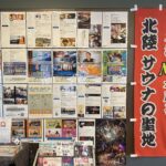 温浴施設の壁面にサウナや水風呂に関する多数の掲示物と赤い垂れ幕が飾られています。