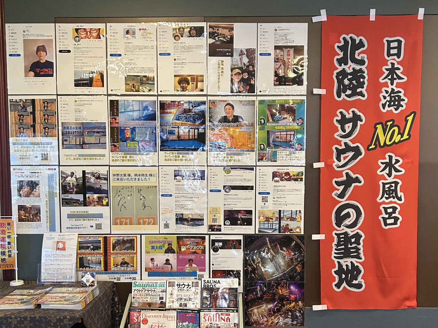 温浴施設の壁面にサウナや水風呂に関する多数の掲示物と赤い垂れ幕が飾られています。