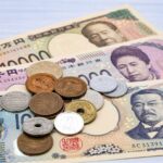白い木目調のテーブルの上に扇状に並べられた日本の新紙幣と複数の硬貨