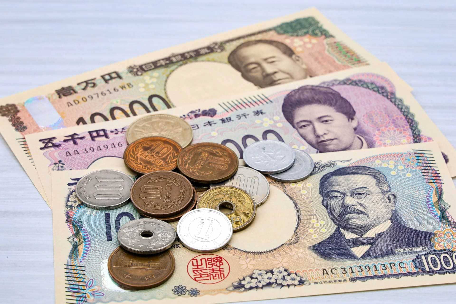 白い木目調のテーブルの上に扇状に並べられた日本の新紙幣と複数の硬貨