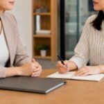 オフィスのデスクでノートを広げてペンを持ち対面で面談を行う様子です