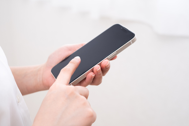 スマートフォンを両手で持ち、画面を指で操作しています。