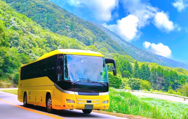 青空と緑豊かな山道沿いを走行する黄色の観光大型バス。