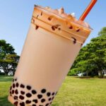 緑豊かな公園の風景を背景に配置されたタピオカミルクティーの画像