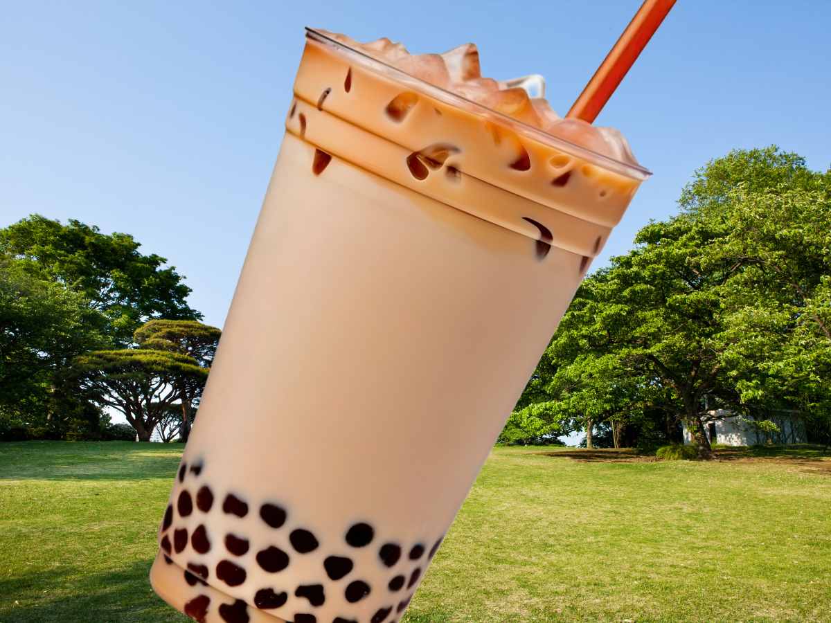 緑豊かな公園の風景を背景に配置されたタピオカミルクティーの画像