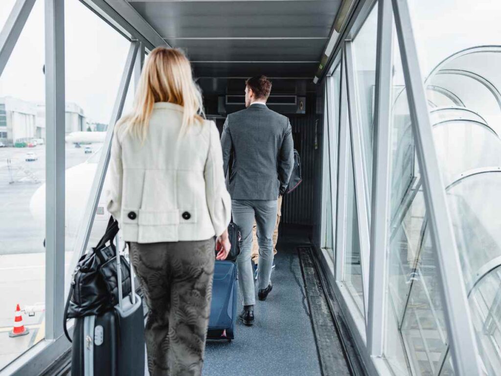 旅行用のスーツケースを引きながら空港の搭乗橋を歩いていく男女の後ろ姿です。