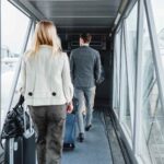 旅行用のスーツケースを引きながら空港の搭乗橋を歩いていく男女の後ろ姿です。