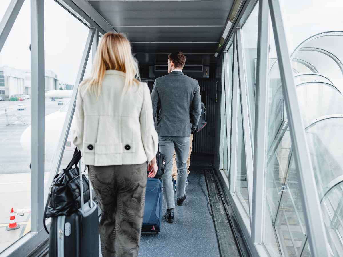 旅行用のスーツケースを引きながら空港の搭乗橋を歩いていく男女の後ろ姿です。