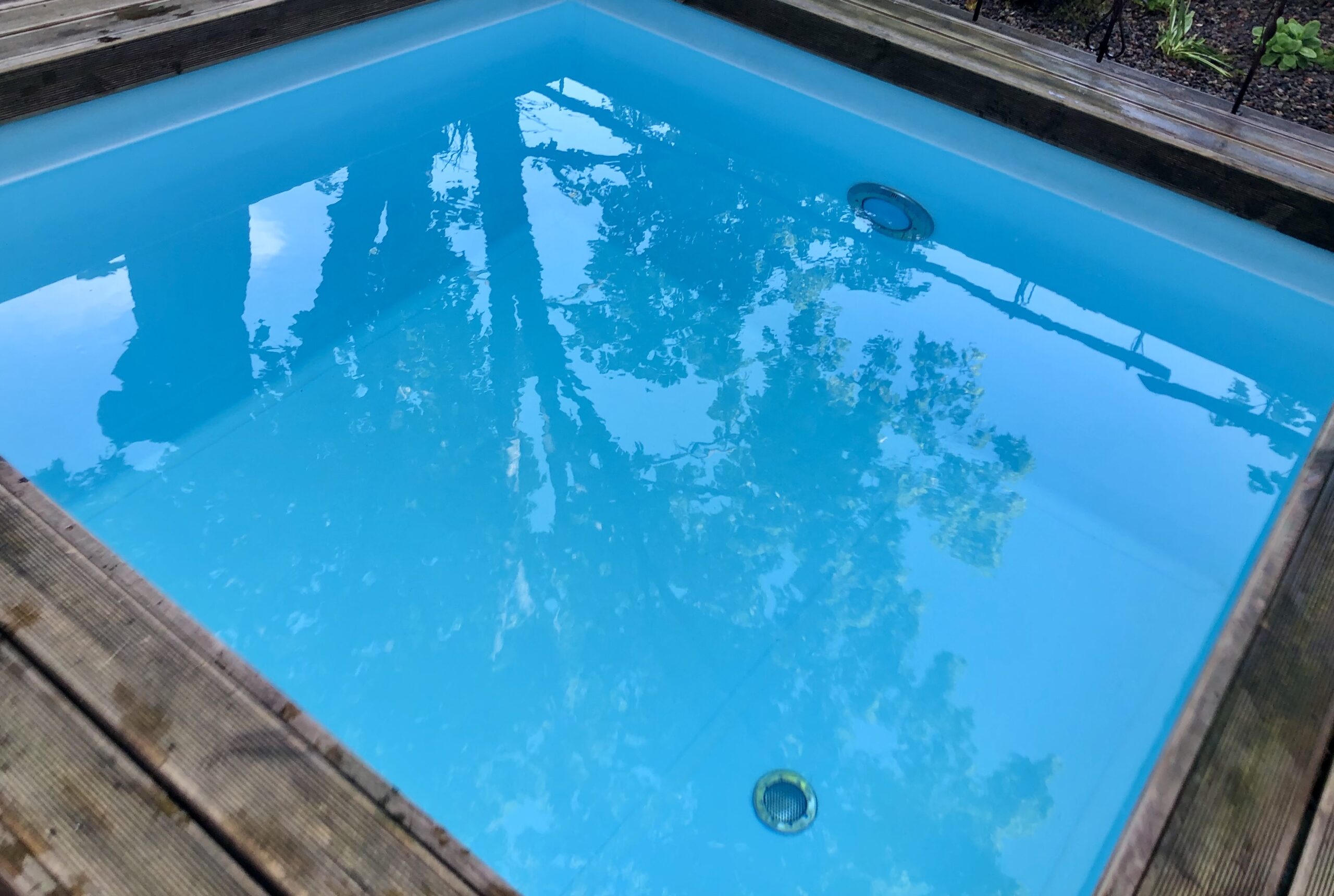 木製のデッキに囲まれた浴槽に青く澄んだ水が張られている屋外の水風呂です。