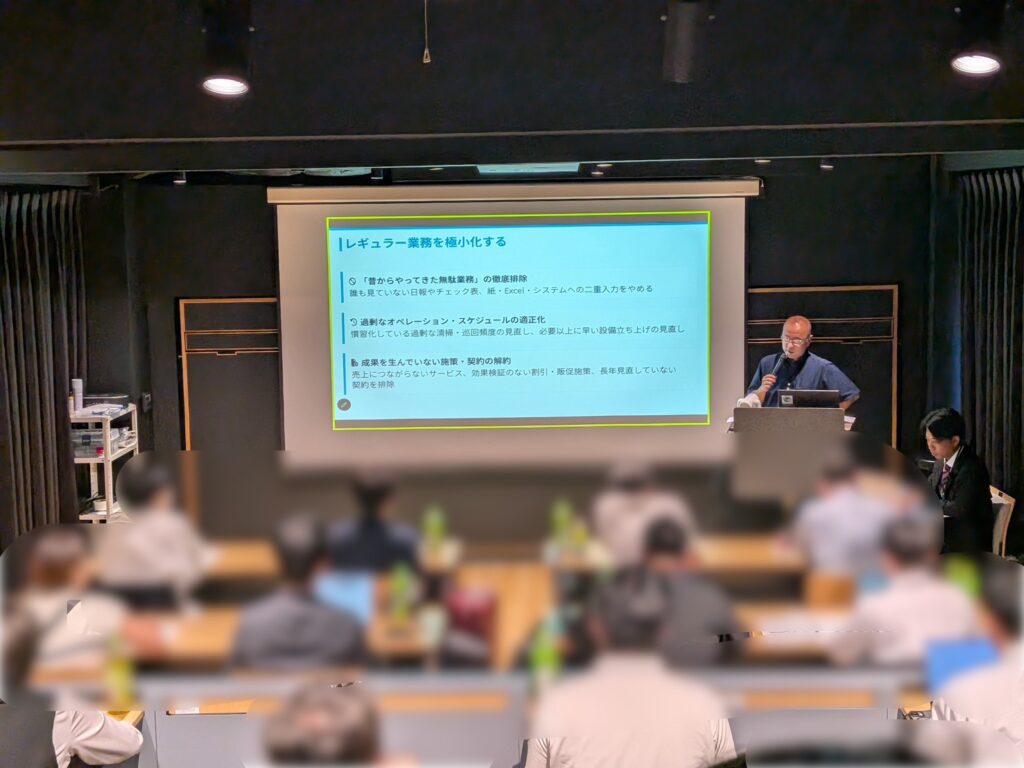 セミナー会場でスライドを背に登壇者がマイクを持って講義を行う様子。