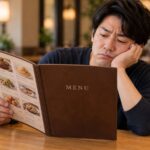 飲食店の席で、男性が頬杖をつきながらメニューブックの料理写真を眺めている。