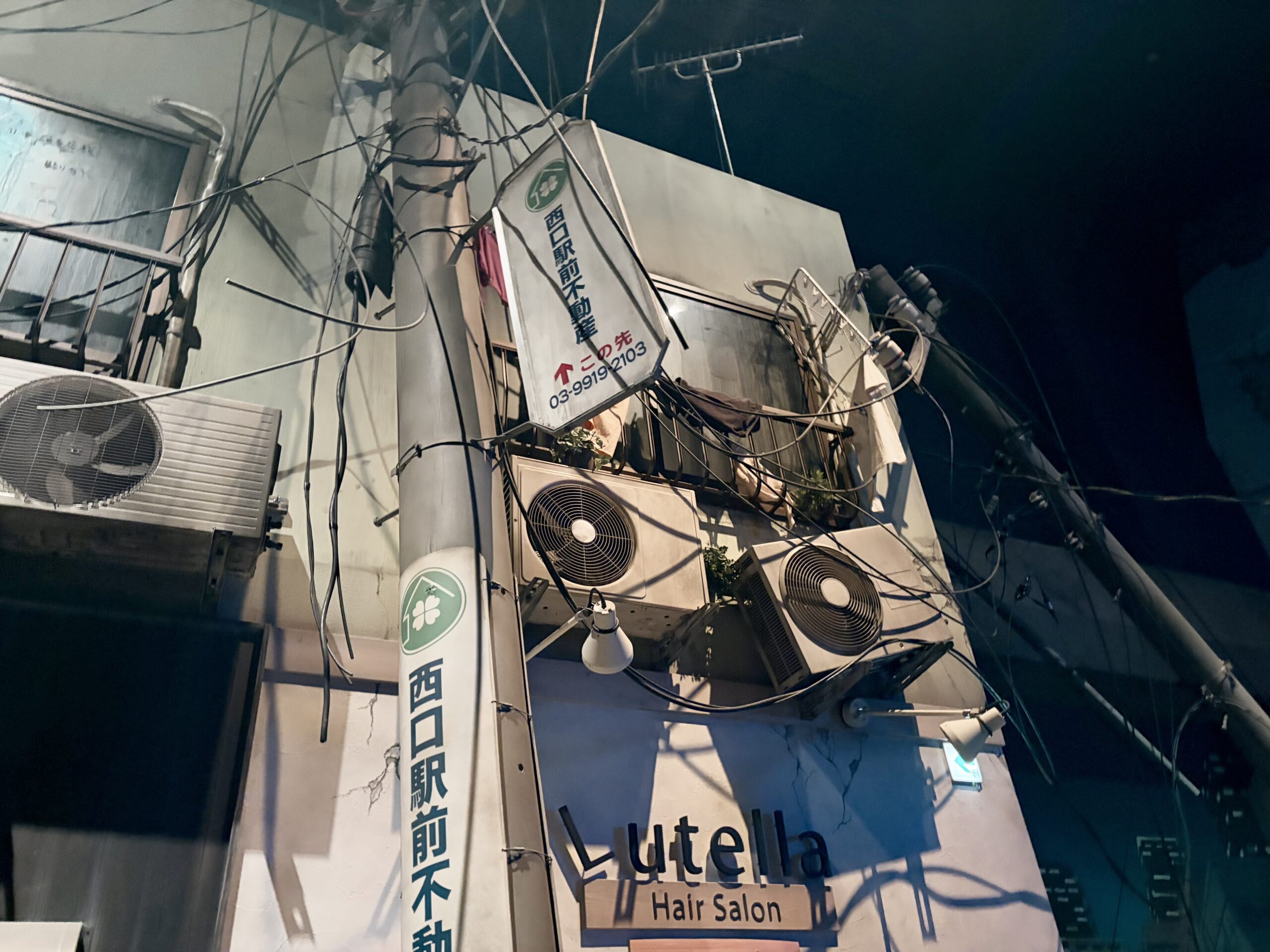 防災体験施設で再現された被災後の街並みで、傾いた電柱と垂れ下がった電線、ひび割れた建物の外壁が写っている。